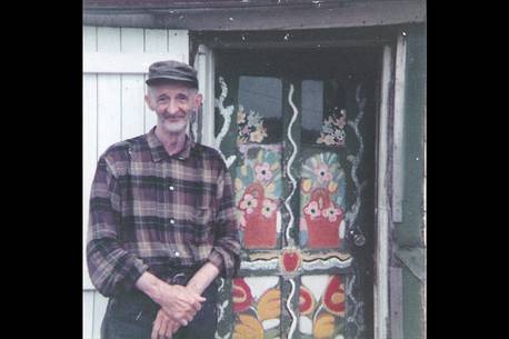 Maud Lewis - Everett standing by the front painted window of the house.png